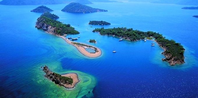 Havadan çekilmiş, yemyeşil bitki örtüsüyle kaplı adaların ve mavi denizin manzarası.