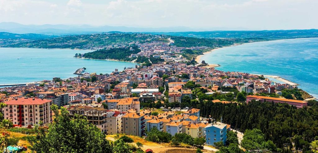 Deniz manzaralı bir tepe üzerinde yer alan bir şehir manzarası, renkli binalar ve yeşil alanlar ile birlikte.