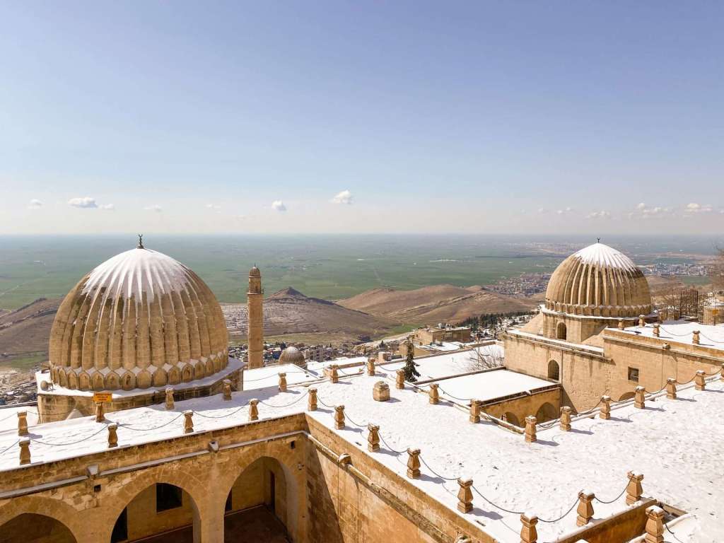 Karla kaplı kubbelerin ve yüksekteki manzaranın görüldüğü tarihi bir yapı.