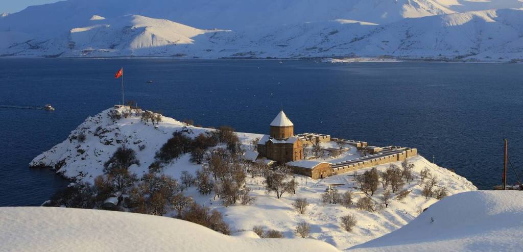 Van Gölü kıyısında, karla kaplı bir adacık üzerinde yer alan tarihi bir yapı ve Türk bayrağı.