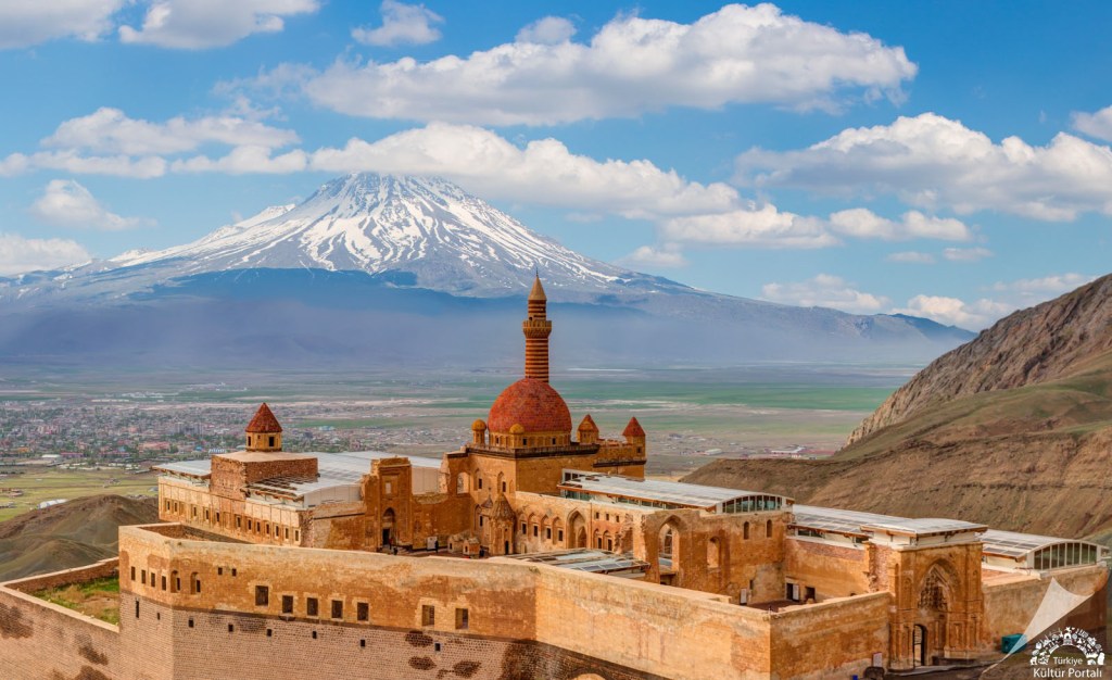 Görsel, Ağrı Dağı'nın arka planda yer aldığı İshak Paşa Sarayı'nın ön planını gösteriyor. Sarayın tarihi yapısı ve dağın karla kaplı zirvesi etkileyici bir manzara oluşturuyor.