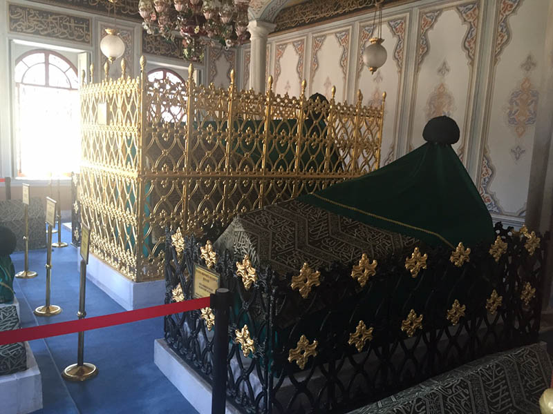 İstanbul'da Aziz Mahmud Hüdayi Türbesi'nin iç kısmı, yeşil örtülerle kaplı mezarların ve süslü demir parmaklıkların bulunduğu tarihi bir mekandır.