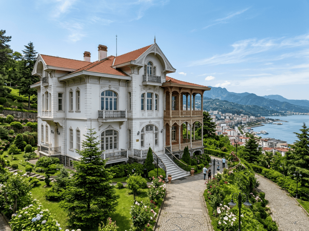 Historic white mansion with red roof, intricate balcony, surrounded by green gardens, overlooking sea and city